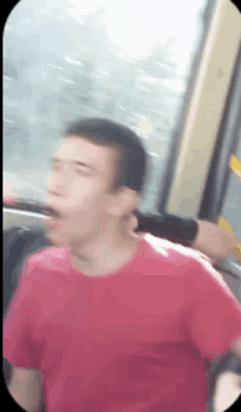 a man in a red shirt is sitting on a bus with his mouth open