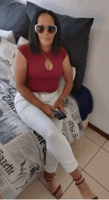 a woman wearing sunglasses sits on a bed with a newspaper cover