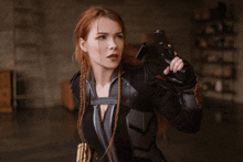 a woman in a black suit holds a gun in her right hand