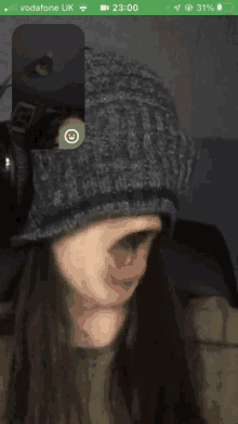 a woman wearing a beanie is on a video call with a smiley face on her phone