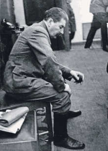 a black and white photo of a man sitting on a stool with his legs crossed