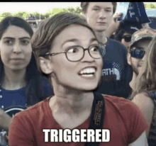 a woman wearing glasses and a red shirt is standing in a crowd of people and making a funny face .