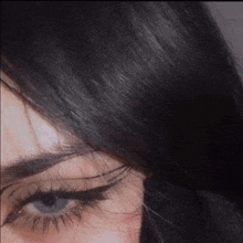 a close up of a woman 's face with long black hair and blue eyes with eyeliner .