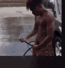 a man without a shirt is washing a car with a hose .