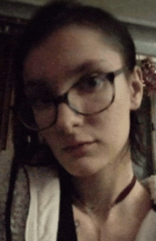 a young woman wearing glasses and a choker looks at the camera