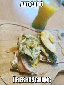 a sandwich with avocado and eggs is on a cutting board with a glass of orange juice in the background