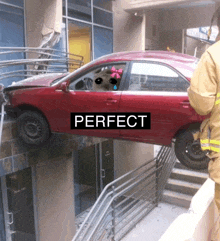 a red car is stuck in a building and the word perfect is on it