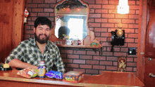 a man in a plaid shirt stands behind a counter with snacks and a box of fireworks that says papa johns on it