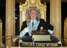 a man in a masonic robe is sitting in a chair holding a hammer .