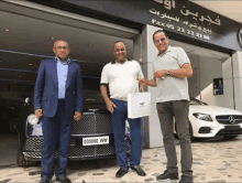 three men are standing next to each other in front of a car dealership .