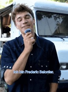 a man in a denim shirt stands in front of a white truck with the words ich bin frederic balonier below him