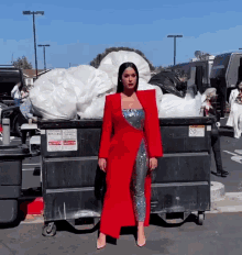 a woman in a red dress is standing in front of a dumpster that has a warning sign on it