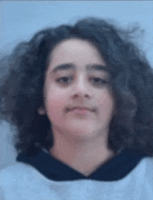 a young girl with long curly hair is wearing a hoodie .