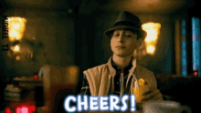 a man in a hat is holding a glass of orange juice and says cheers !