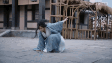 a man in a blue kimono is kneeling on the ground in front of a building that says youku on it