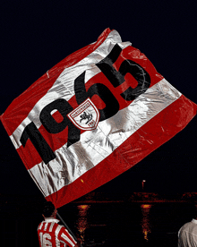 a man holds up a red and white flag that says 1965