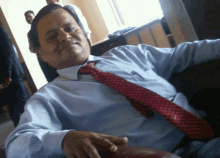 a man in a blue shirt and red tie sits on a chair