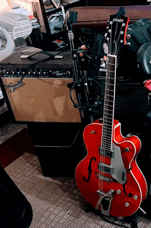 a red greisch guitar sits on a stand in front of an amplifier