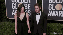 a man and a woman holding hands on a red carpet in front of a sign that says golden globe awards