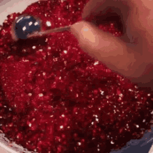 a person is scooping a blue ball into a pile of red glitter .