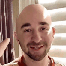 a bald man with a beard is smiling and pointing at the camera while wearing a red shirt .