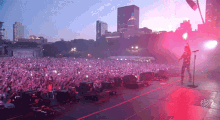 a man singing into a microphone in front of a crowd at a concert with a city in the background