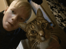 a young boy holds a cat in his arms and the cat looks at the camera