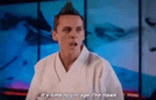 a man in a white karate uniform is sitting in front of a blue screen .