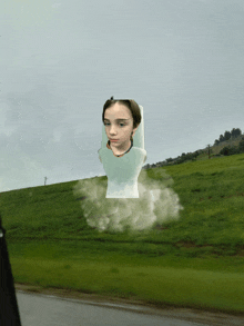 a picture of a girl is floating in the air in front of a grassy hill