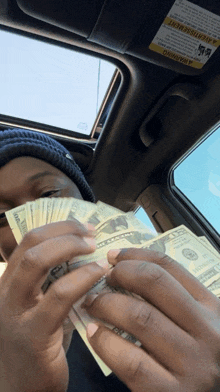 a person in a car holding a bunch of money with a warning sticker on the visor