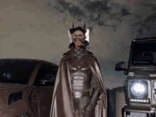 a man in a batman costume is wearing a mask and standing next to a jeep .