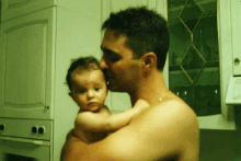 a shirtless man is holding a baby in his arms in a kitchen