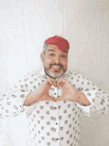 a man with pink hair is making a heart shape with his hands in front of a white wall