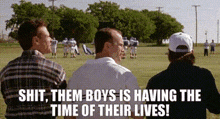 three men are standing in a field watching a football game and one of them is talking about the time of their lives .