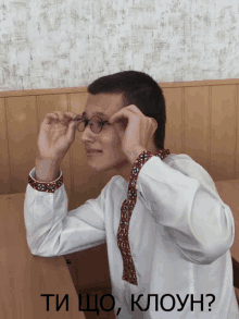 a man wearing glasses is sitting at a desk with the words ti cho klouh on the bottom right