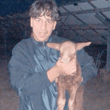 a man in a blue jacket is holding a small brown animal