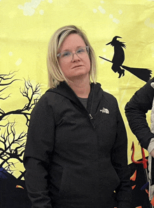 a woman wearing a black north face jacket stands in front of a yellow background