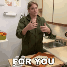 a woman in a green jumpsuit stands in a kitchen with a tray of food and the words " for you " on the counter