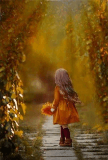 a little girl in a yellow dress is walking down a path holding a bunch of leaves .