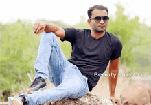 a man wearing sunglasses sits on a rock in front of a beauty plus cam sign