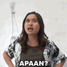 a woman is standing in front of a shower head and making a funny face with the word apaan written on it .