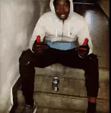 a man in a hoodie is sitting on a set of stairs with a can of soda in front of him