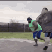 a group of men are running on a road . one of the men is wearing a green shirt and blue shorts .