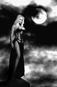 a woman in a long black dress is standing in front of a full moon .