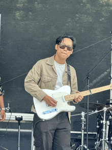 a man wearing sunglasses is playing a guitar with a strap that says ' fender ' on it