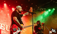 a man singing into a microphone while another man plays a guitar in front of a sign that says bad crew