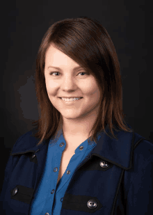 a woman wearing a blue shirt and a blue jacket smiles for the camera