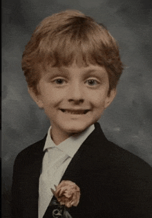 a young boy wearing a suit and tie with a flower pin on his lapel .