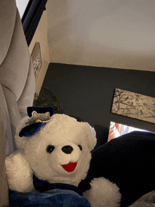 a white teddy bear with a blue bow on its head is sitting on a bed