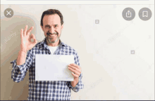 a man in a plaid shirt is holding a piece of paper and giving an okay sign